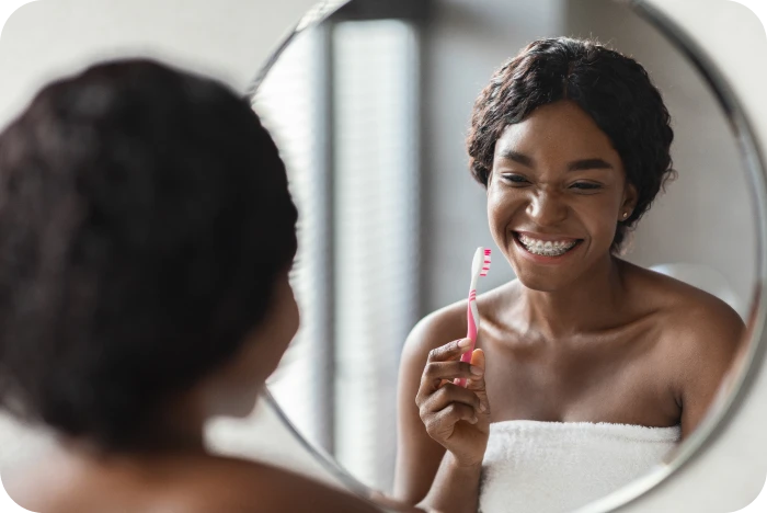Patiente avec appareil multi-attaches se brossant les dents devant un miroir