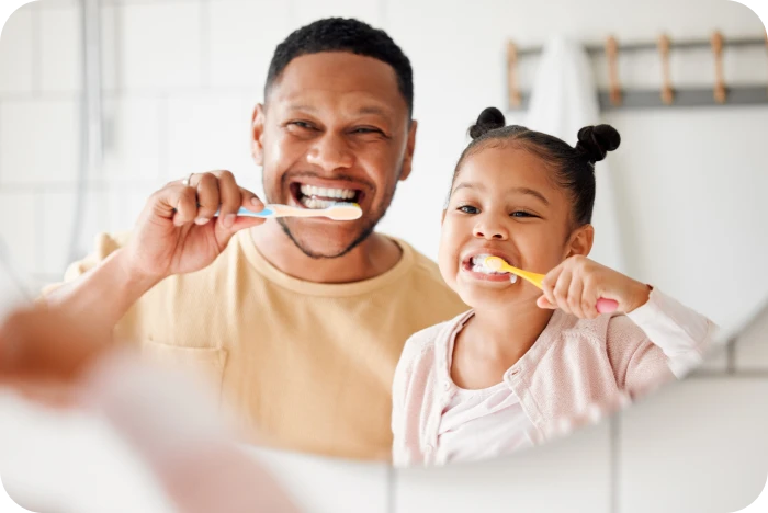 Père et enfant se brossant les dents ensemble devant un miroir